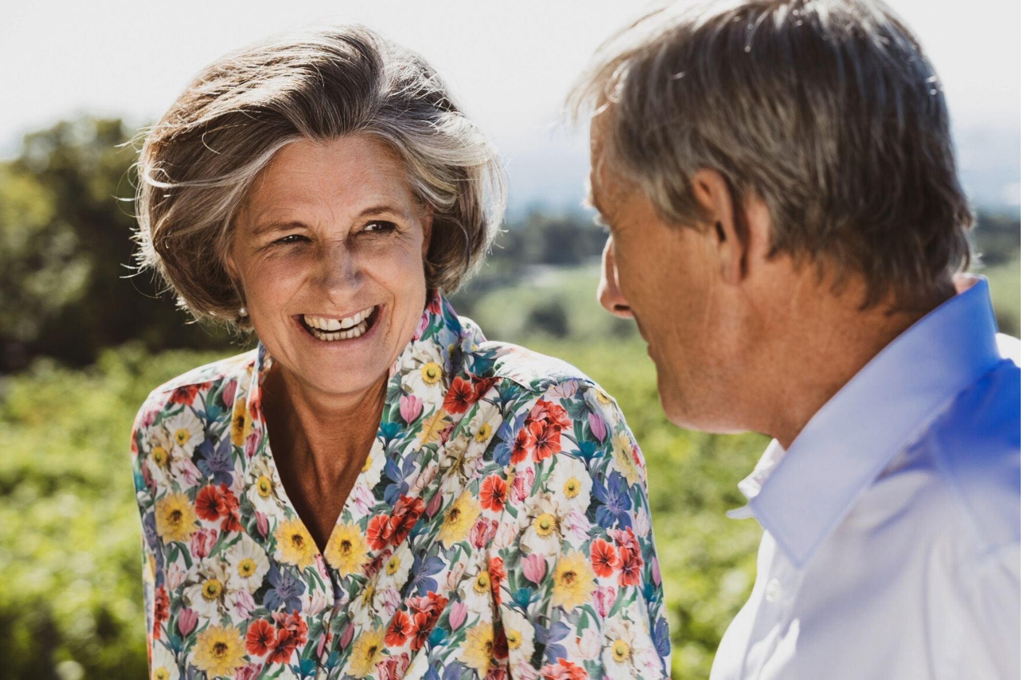 Dame strahlt Herren an. Sie trägt eine blumige Bluse mit Magnetverschlüssen, er ein weißes Hemd mit Magnetverschluss.